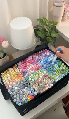 a person is holding a marker in front of a large tray of colored crayons