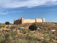 people are walking around in the desert near an old castle with flags on it's walls