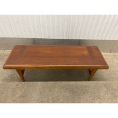 a wooden coffee table sitting on top of a cement floor next to a white wall