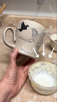 a hand holding a coffee mug with an image of a bird on it and another cup next to it