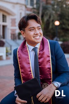 a man in a suit and tie sitting on a bench with his graduation cap over his shoulder