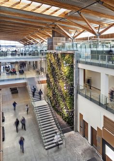 people are walking around an indoor building with plants growing on the wall and stairs to the second floor