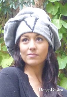 a woman wearing a gray hat standing in front of some trees and leaves with her eyes closed