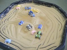 there are many toy trucks and cars in the sand on this play tray for toddlers