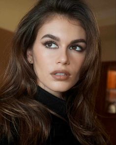 a woman with long brown hair and blue eyes is posing for the camera, wearing a black turtle neck top