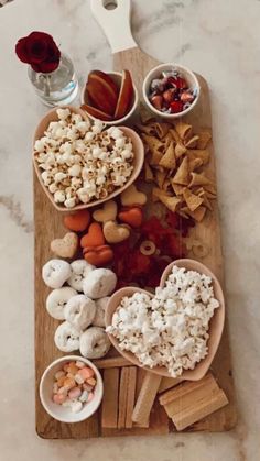 a wooden cutting board topped with bowls filled with food next to crackers and chips