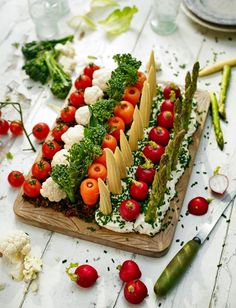 a wooden cutting board topped with lots of veggies on top of a table