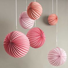 three pink and white paper fans hanging from strings on the wall next to each other