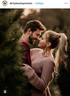 a man and woman standing next to each other in front of pine trees at sunset