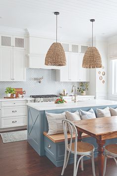 a kitchen with white cabinets and blue island in the center, surrounded by wicker pendant lights