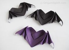 three origami bats are shown on a white surface, one is black and the other is purple