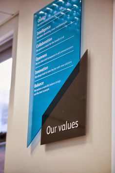 a blue sign hanging on the side of a wall next to a window in an office