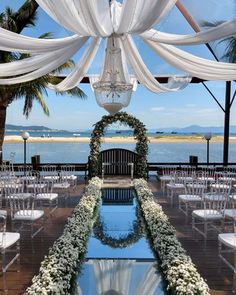 an outdoor ceremony setup with white drapes and flowers on the ground, along with chairs