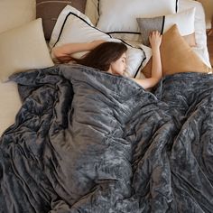 a woman laying in bed under a blanket with pillows on top of her and one hand up to her head