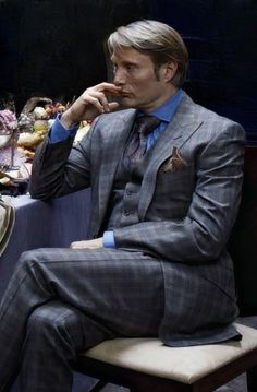 a man in a suit sitting at a table with other people around him eating food