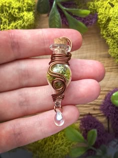 a hand holding a wire wrapped pendant with green and white glass beads on it's end