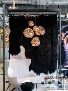 a white chair sitting in front of a black and white wall with lights hanging from it