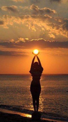 a woman is standing on the beach with her hands in the air as the sun sets