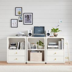 a white bookcase with books, speakers and pictures on the wall in front of it