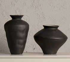 two black vases sitting on top of a white shelf