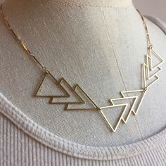 a gold necklace on a mannequin neck with geometric shapes hanging from it's sides