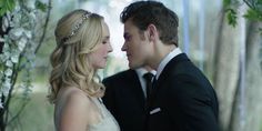 a bride and groom kissing in front of an arch with flowers on the wall behind them