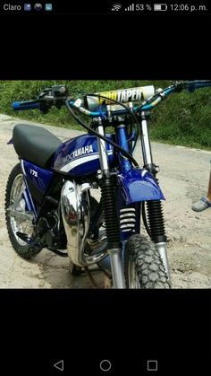 a blue motorcycle parked on top of a dirt road next to a person standing in the background