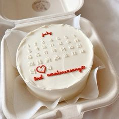 a white cake with red writing on it in a plastic container next to an open box