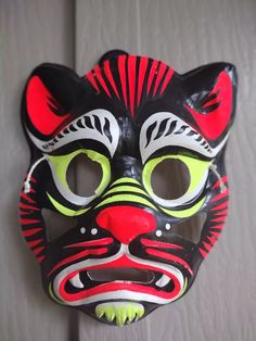 a black and red mask with green eyes on a white surface, in the shape of a tiger's head