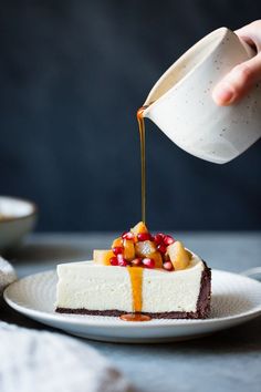 someone pouring syrup on a piece of cheesecake with pomegranate and fruit