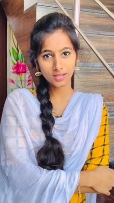 a woman with long black hair wearing a yellow and white sari is standing in front of some stairs