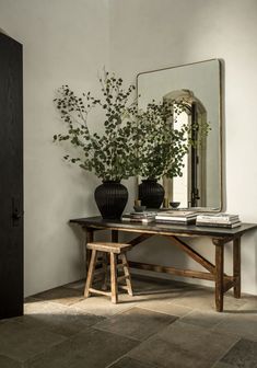 a table with two vases on top of it next to a mirror and plant