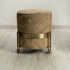 a round ottoman sitting on top of a hard wood floor next to a white wall