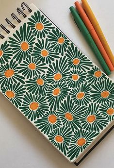 a notepad with an orange and green flower design on it next to two colored pencils