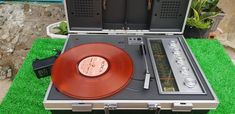 an old fashioned record player and radio in a suitcase on the grass next to some plants