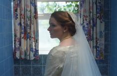 a woman in a wedding dress is looking out the window with her veil pulled back