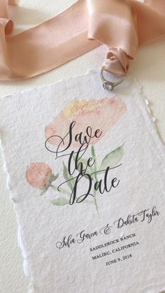 wedding save the date card with pink ribbon and ring on it, next to a rose