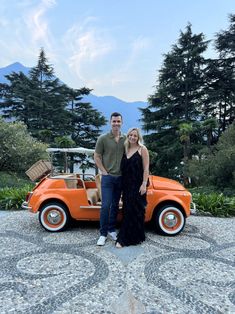 a man and woman standing next to an orange car