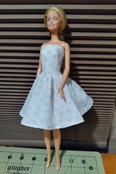 a barbie doll wearing a white dress on top of a table with a ruler in front of it