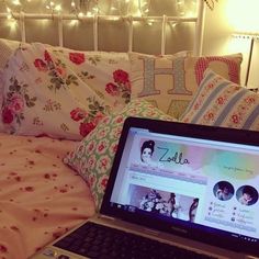 an open laptop computer sitting on top of a bed next to pillows and blankets with lights in the background