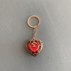 a red heart shaped keychain on a gray surface with a gold chain hanging from it