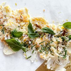 some food is laying on top of a white tablecloth with green leaves and cheese