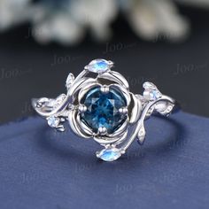 a ring with blue topazte surrounded by leaves and diamonds on a blue cloth