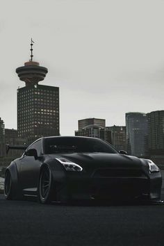 a black sports car parked in front of a tall building with a tower behind it