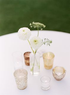 a white table topped with glasses and vases filled with flowers on top of it