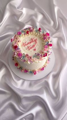 a white cake with pink and blue frosting on top of a white table cloth