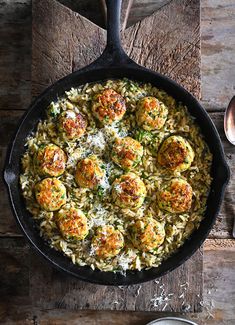 a skillet filled with pasta and meatballs on top of a wooden table next to silverware