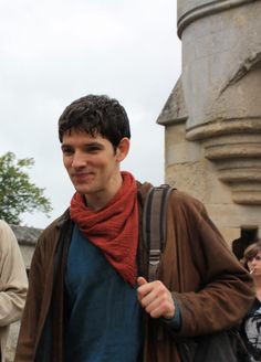 a man with a red scarf around his neck is standing in front of an old building