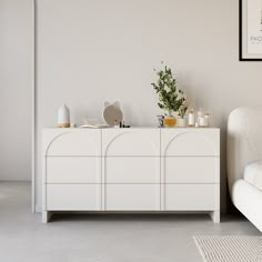 a living room with white furniture and plants on the top of the cabinet, next to a couch