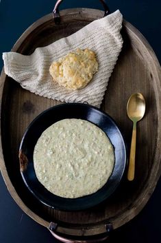 a black plate topped with food next to a spoon and a biscuit on top of a wooden table